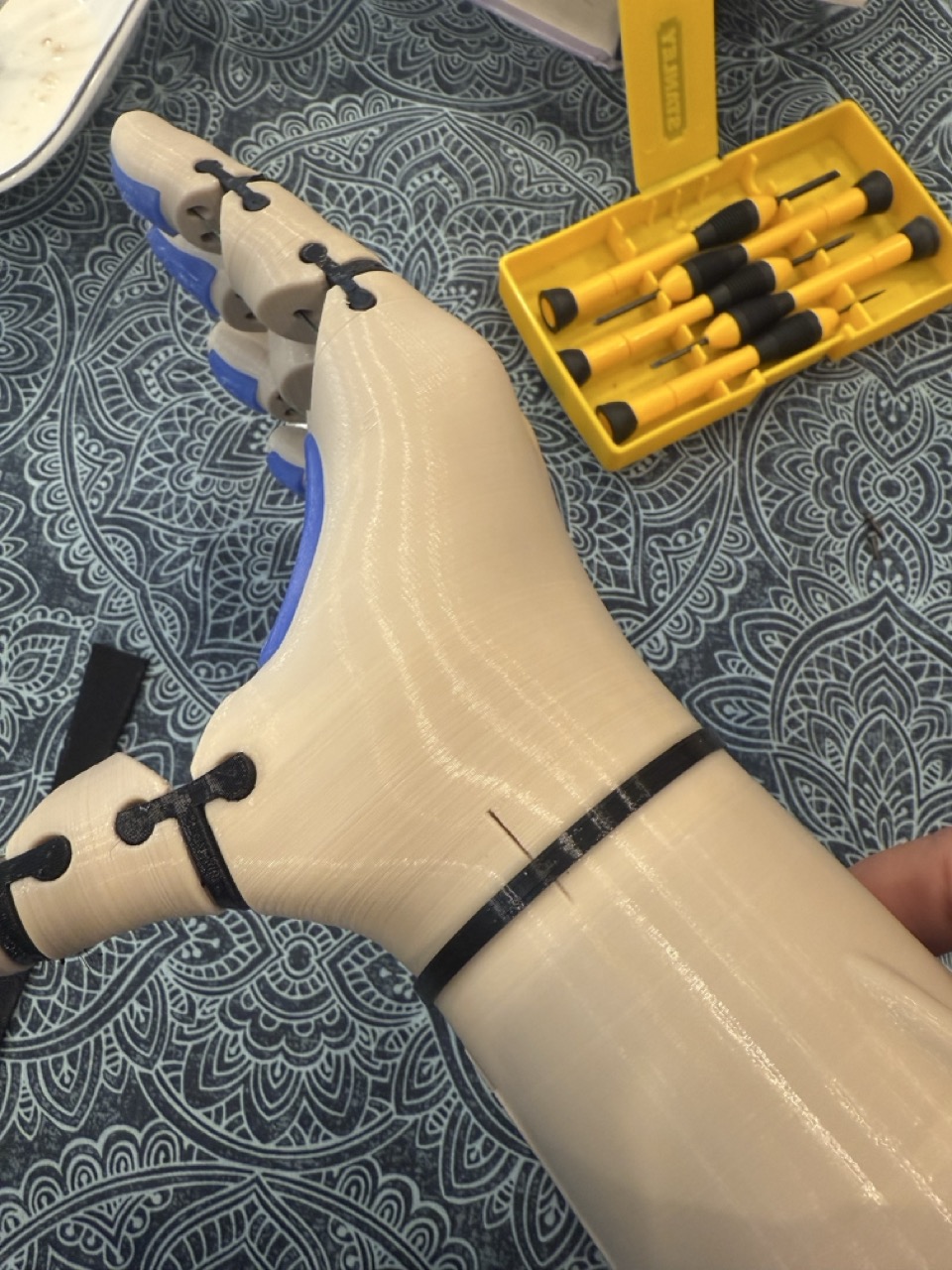 Hand assembly close-up, fingers and palm being fitted, screwdrivers alongside