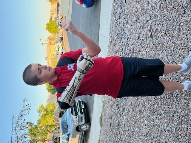 Mi. outside in a red shirt, holding the arm up, delivery day, June 9, 2025