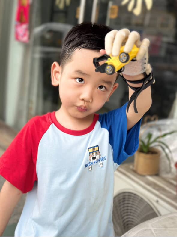 W. holding a toy car high with his prosthetic hand, outdoor