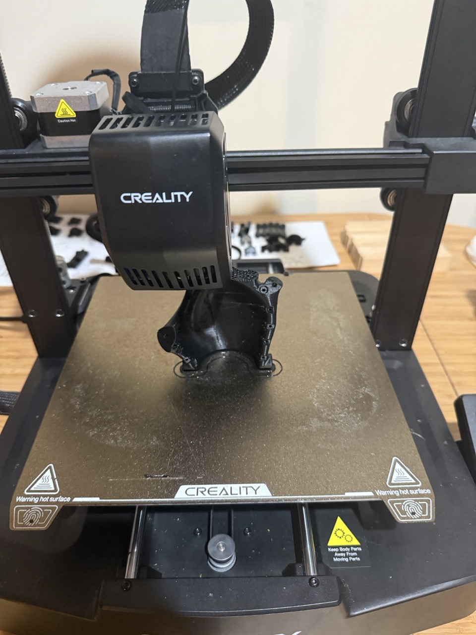 Complex wrist connector piece mid-print showing the curved 3D geometry with pivot points