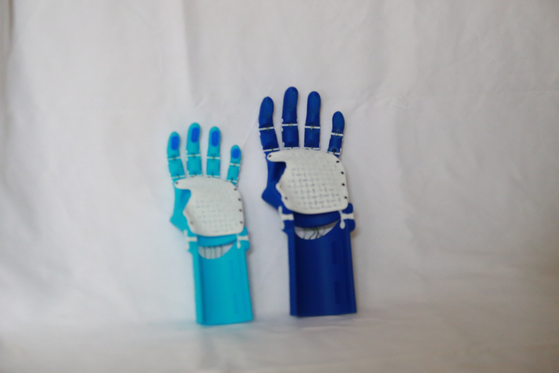 Both completed Thumbless Kinetic Hands standing side by side on white fabric, light blue on the left and dark blue on the right, fingers open