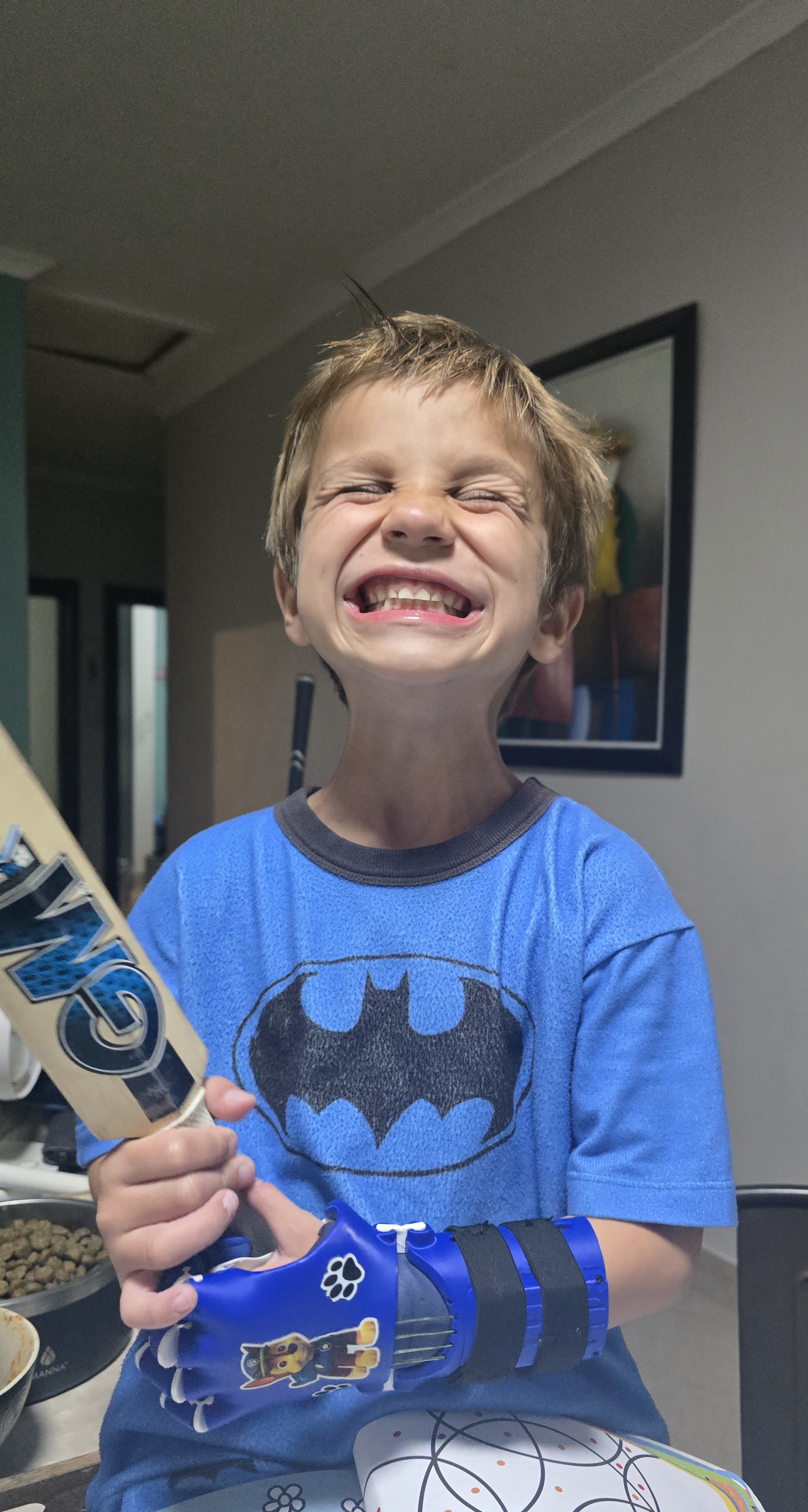 Noah with a huge grin holding the cricket bat with his prosthetic hand, showing pure joy