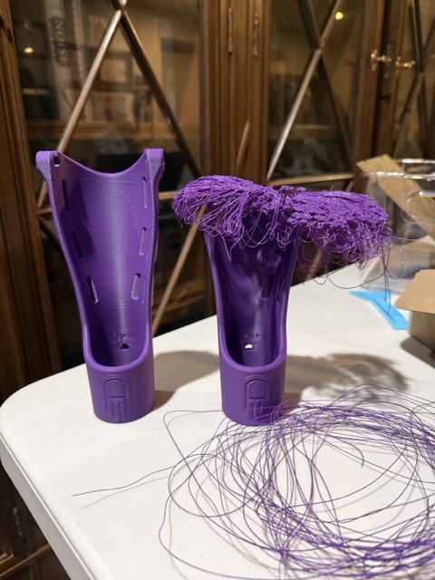 A good purple gauntlet next to a failed one covered in loose filament, sitting side by side on the work table
