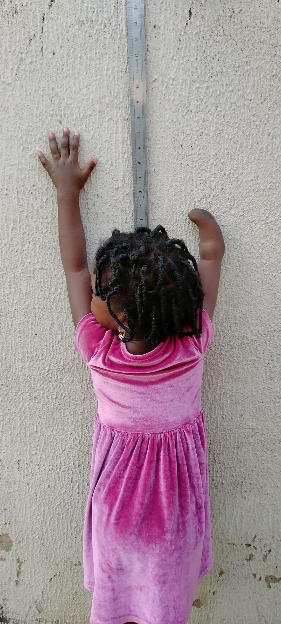 O.C. as a young girl in a pink dress, reaching up against a wall