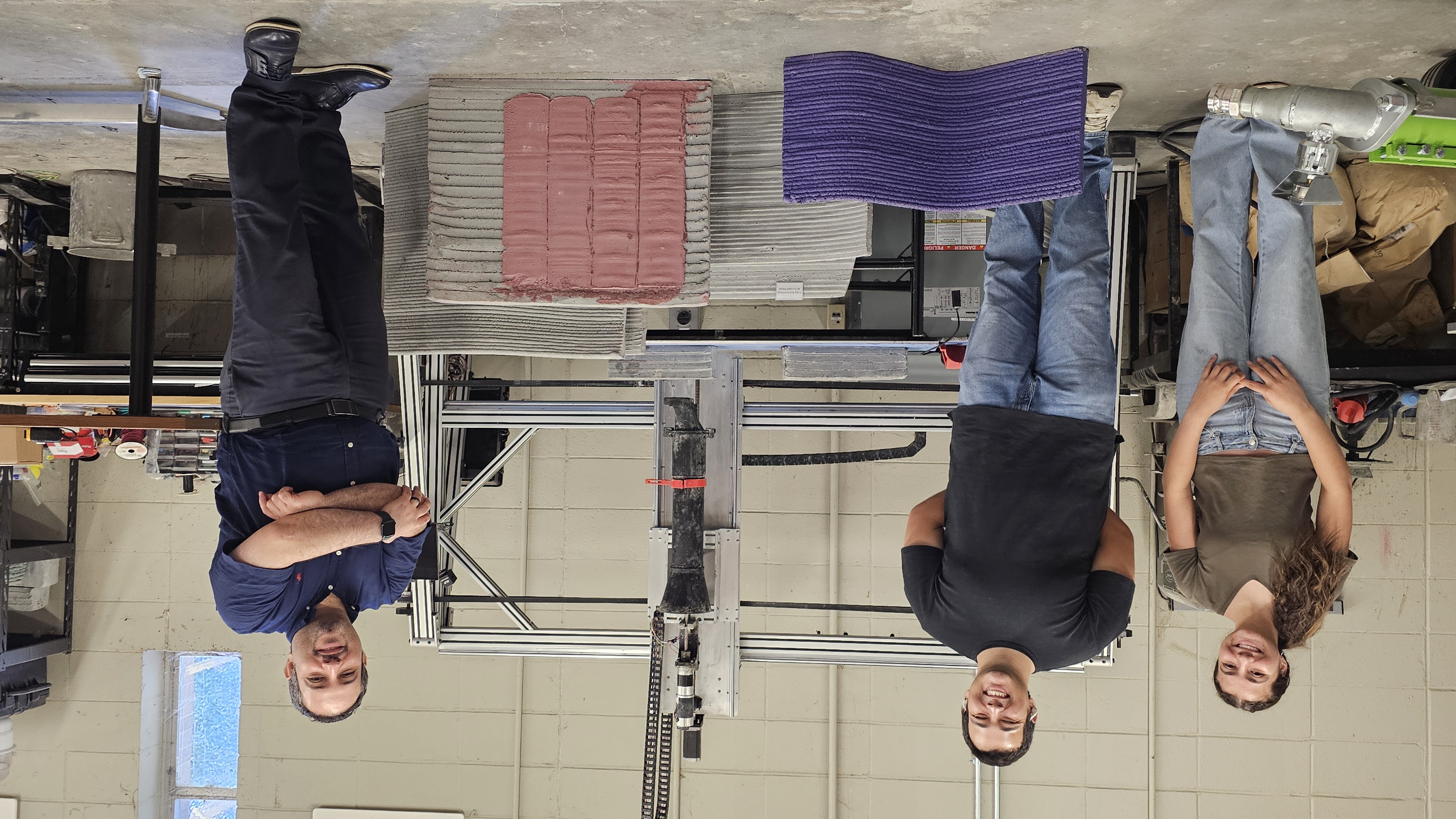 Laila, a graduate student, and Dr. Ali Kazemian in front of the gantry concrete printer with printed concrete and sulfur samples at the RECAST Lab